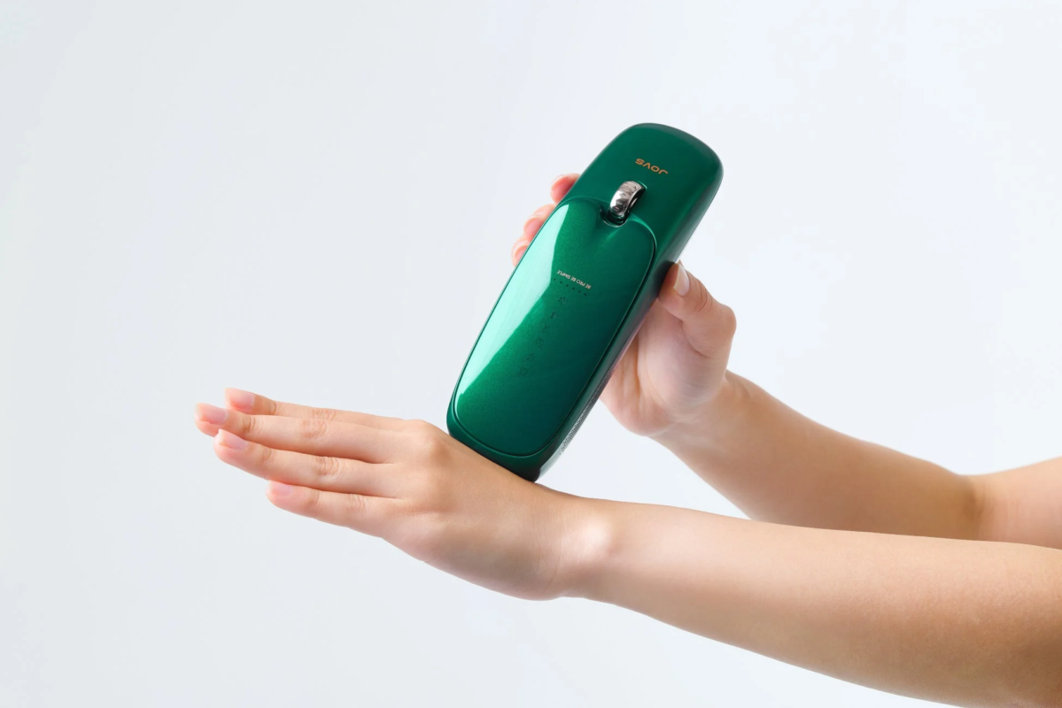 A metallic green stylish beauty device is held with both hands against a white background.