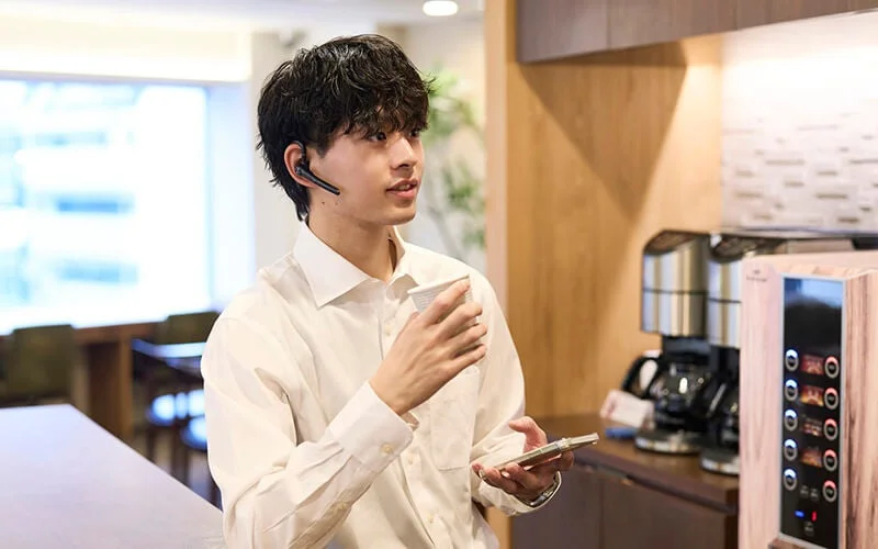 Man in an office using a headset and smartphone during a coffee break