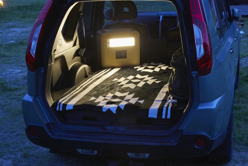 Car trunk open at night with a portable power station and a patterned blanket