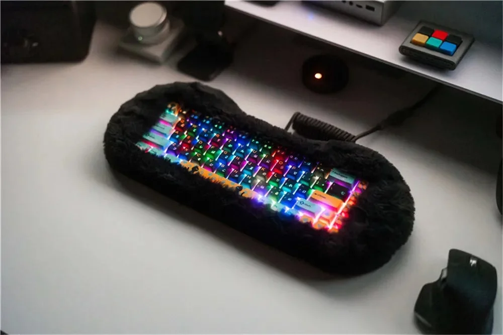 A keyboard with colorful RGB backlighting, encased in a black fluffy material, placed on a desk with a mouse and other gadgets.