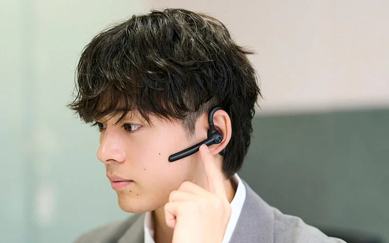 Young man wearing a black wireless headset on his right ear, operating it with his finger