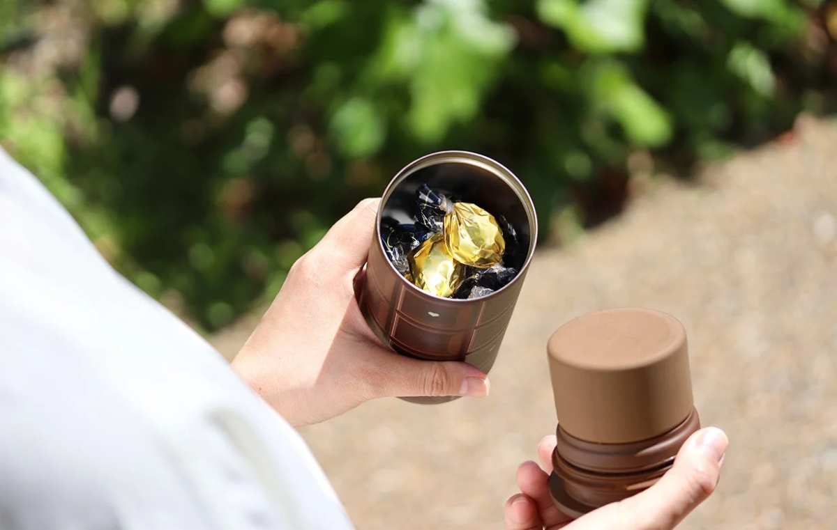 Hand opening a brown container of chocolates outdoors