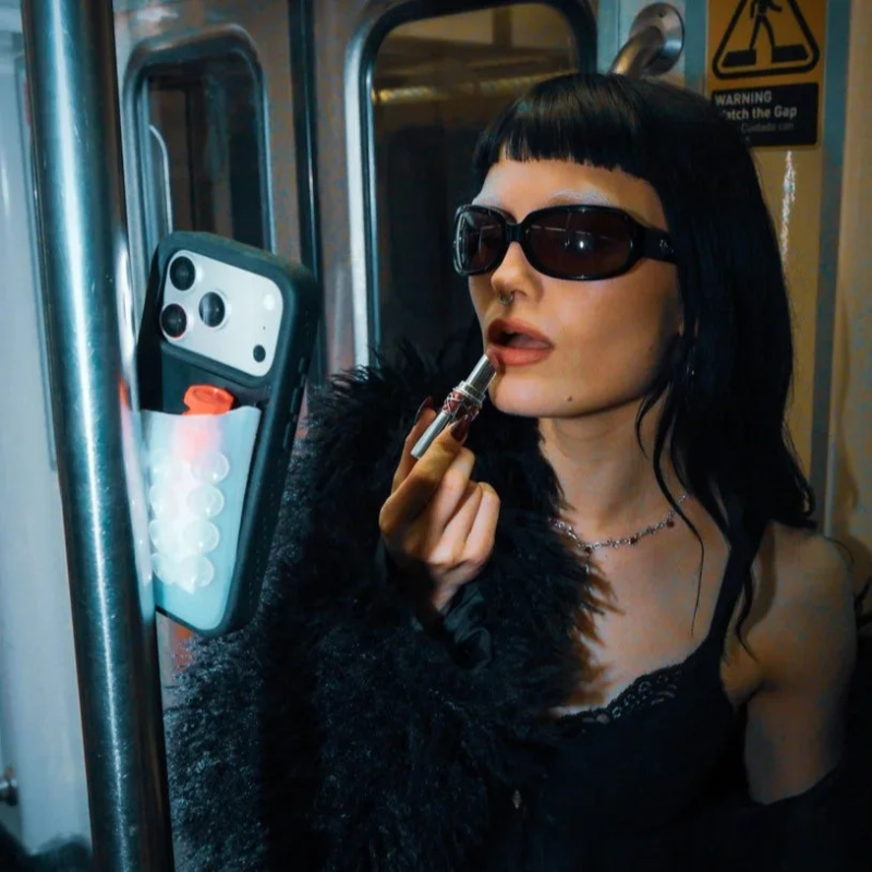 Woman applying lipstick with phone attached to handrail