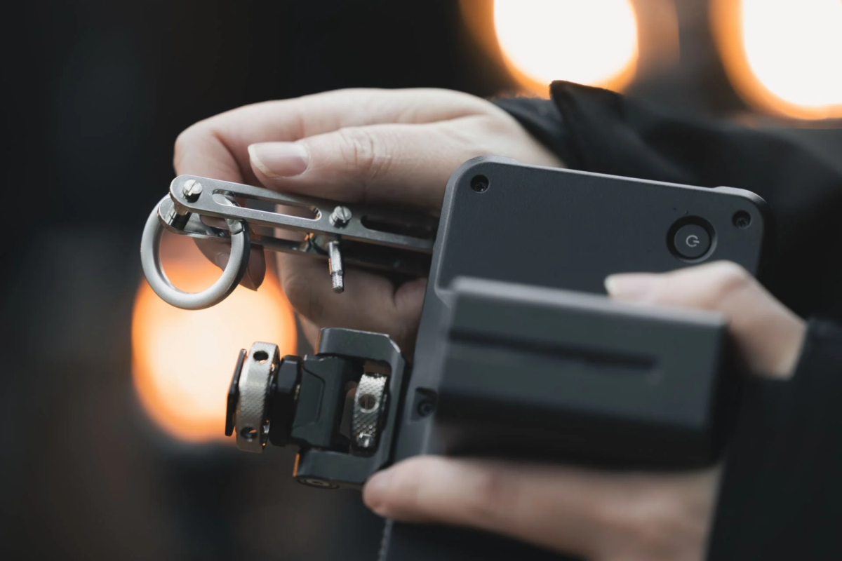 A hand operating camera gear with a metal tool and a black device.