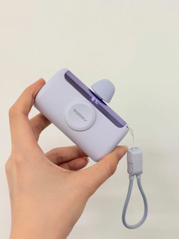 Hand holding a purple and white RORRY portable charger with digital display