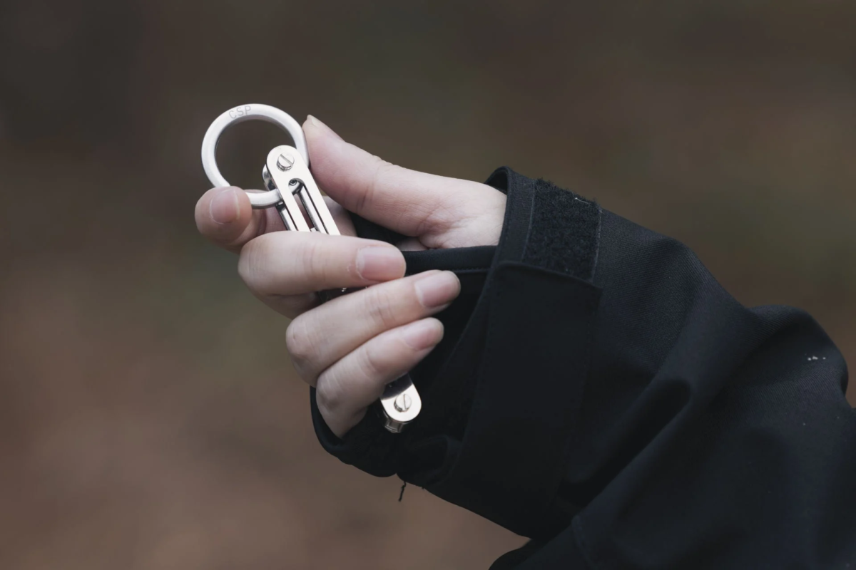 A hand holding a silver keyholder or key organizer.