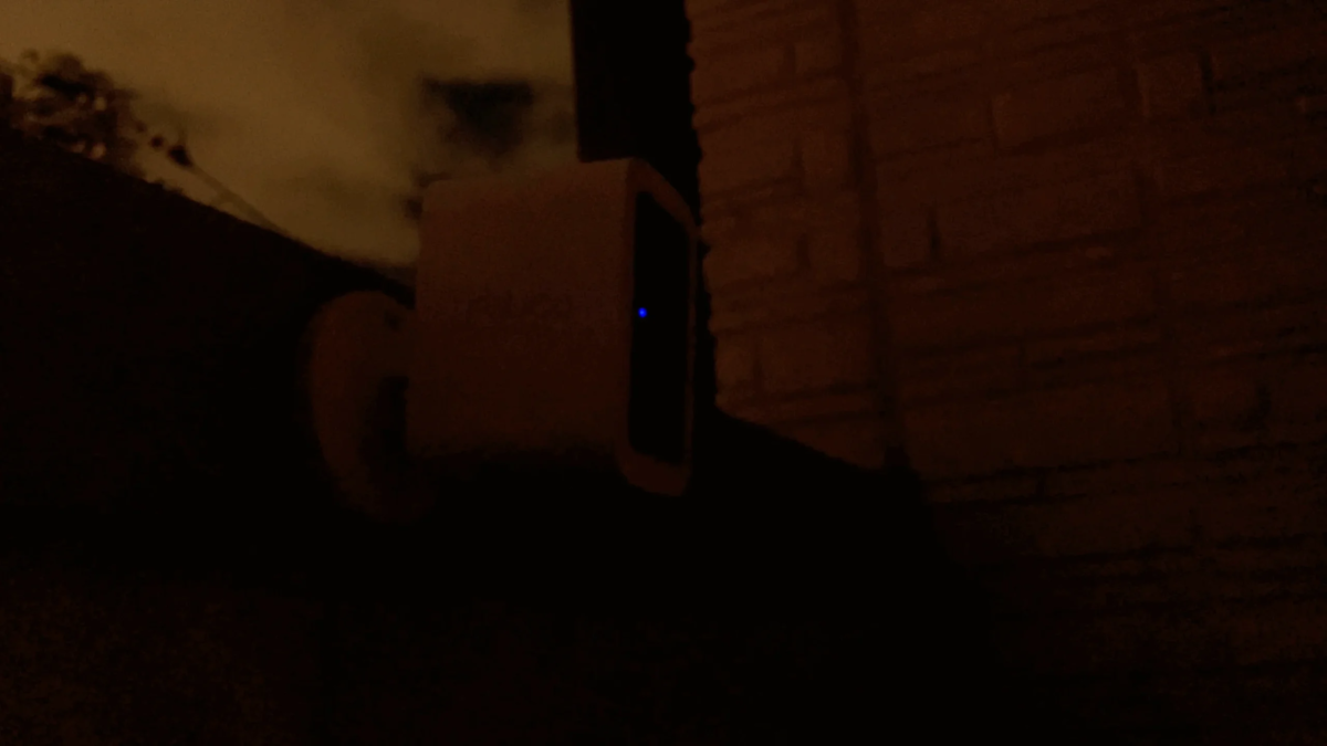 A security camera emits a blue light in the dark, indicating night surveillance.