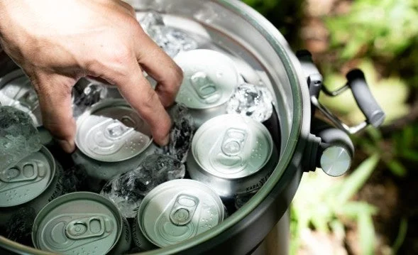 Hand reaching into a cooler box filled with ice and canned drinks