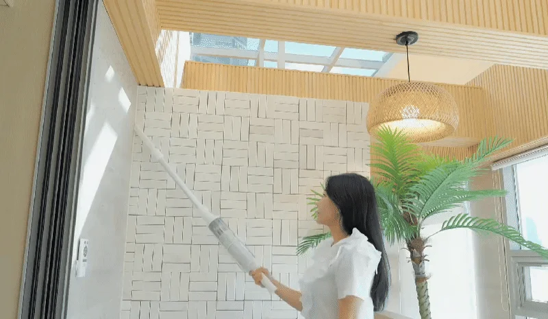Woman cleaning a wall with a white stick vacuum cleaner in a modern living room