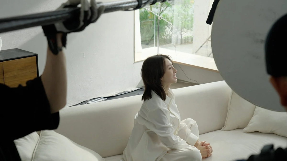 Woman on a white sofa, smiling upwards, with production equipment visible