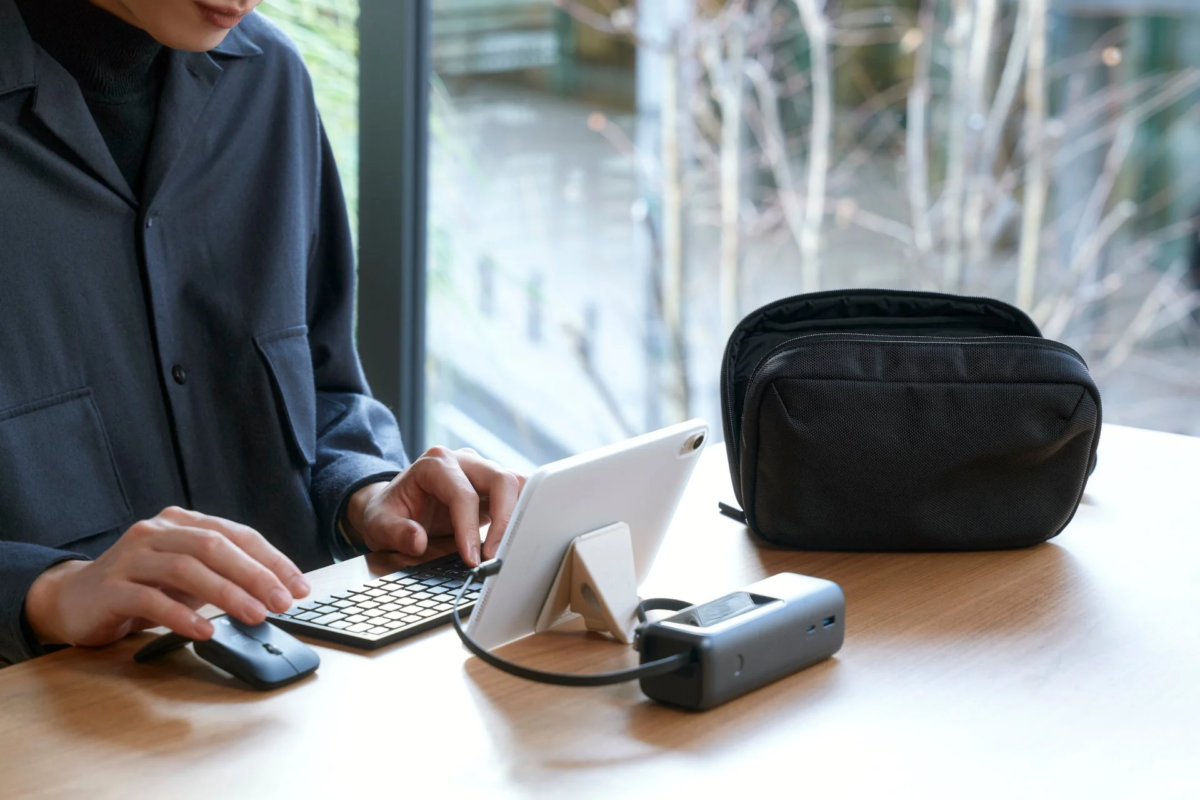 A person working at a desk with a tablet, keyboard, mouse, charger, and the black gadget pouch