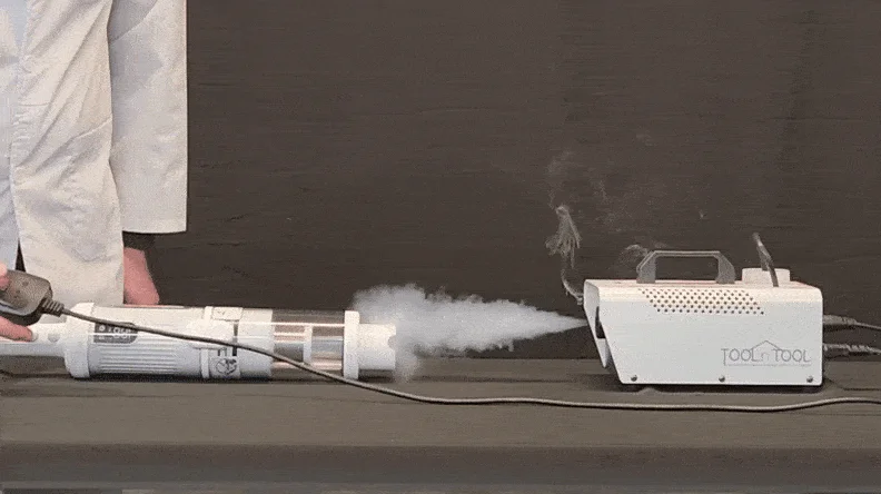 Smoke being emitted from a white fog machine into a transparent pipe-like device