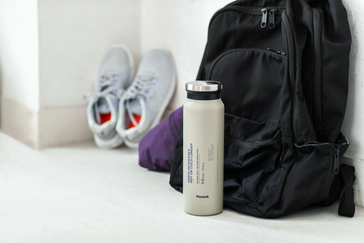 Off-white Peacock stainless steel bottle next to a black backpack