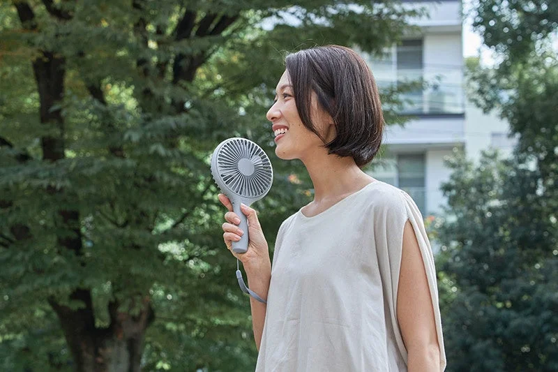 A woman holding the large, uchiwa-sized handy fan to her face