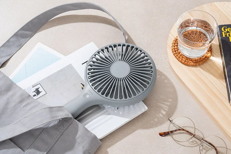 The Uchiwa Handy Fan partially visible from a tote bag, illustrating its portability and double-click power feature