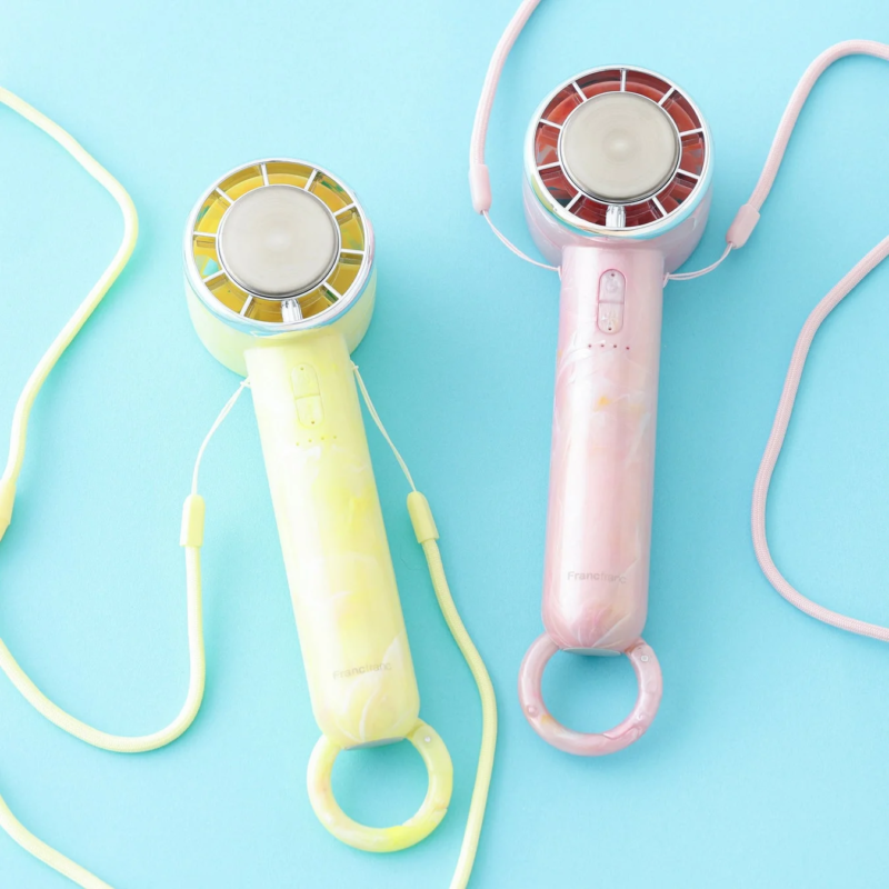 Pink and yellow Francfranc handy fans with straps on blue background