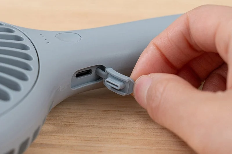 A hand opening the protective cover of the USB-C charging port on the fan