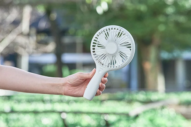 A hand holding the white Uchiwa Handy Fan outdoors, demonstrating its portability