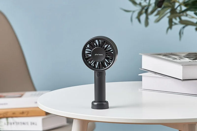 Black handy fan on a desk with a plant