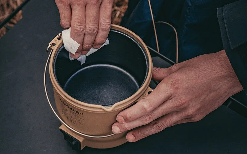 A hand cleaning the inside of a cooker with a tissue-like material outdoors.
