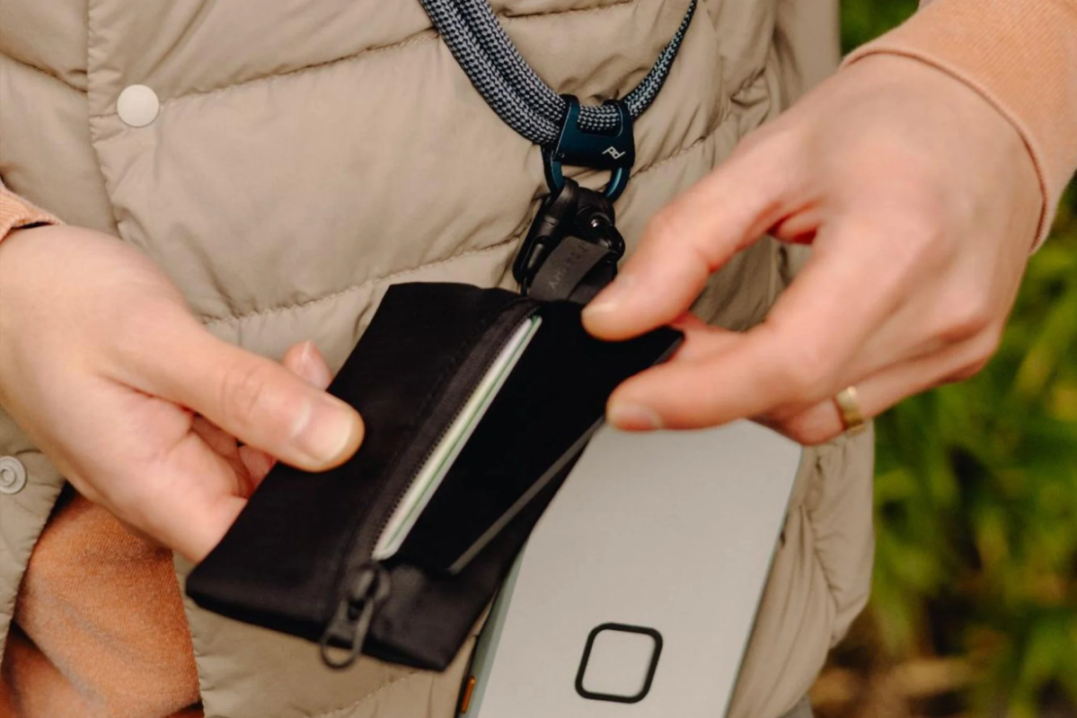 Person holding a smartphone and a pouch with a neck strap