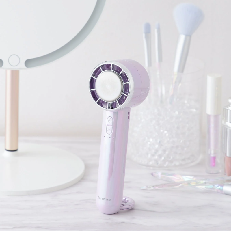 Purple and aurora-colored handy fan on a dresser with makeup brushes