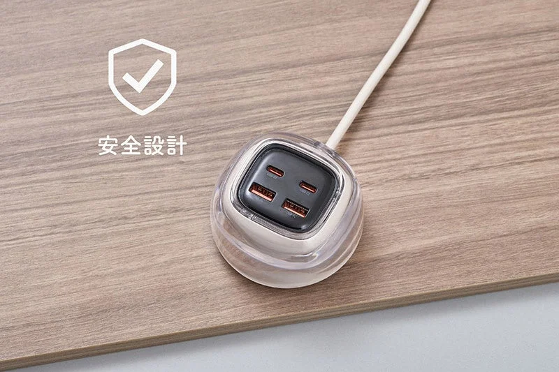 A transparent-cased USB charger with four USB ports on a wooden table, featuring a 'Safety Design' icon.