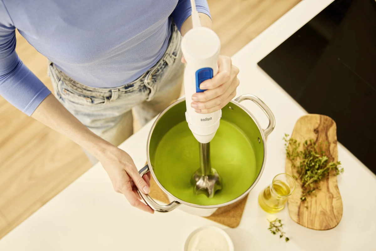 Woman using a Braun hand blender in a green liquid in a large pot