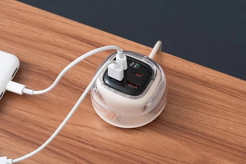A multi-functional USB charging hub on a wooden desk, displaying digital readouts for percentage and wattage.