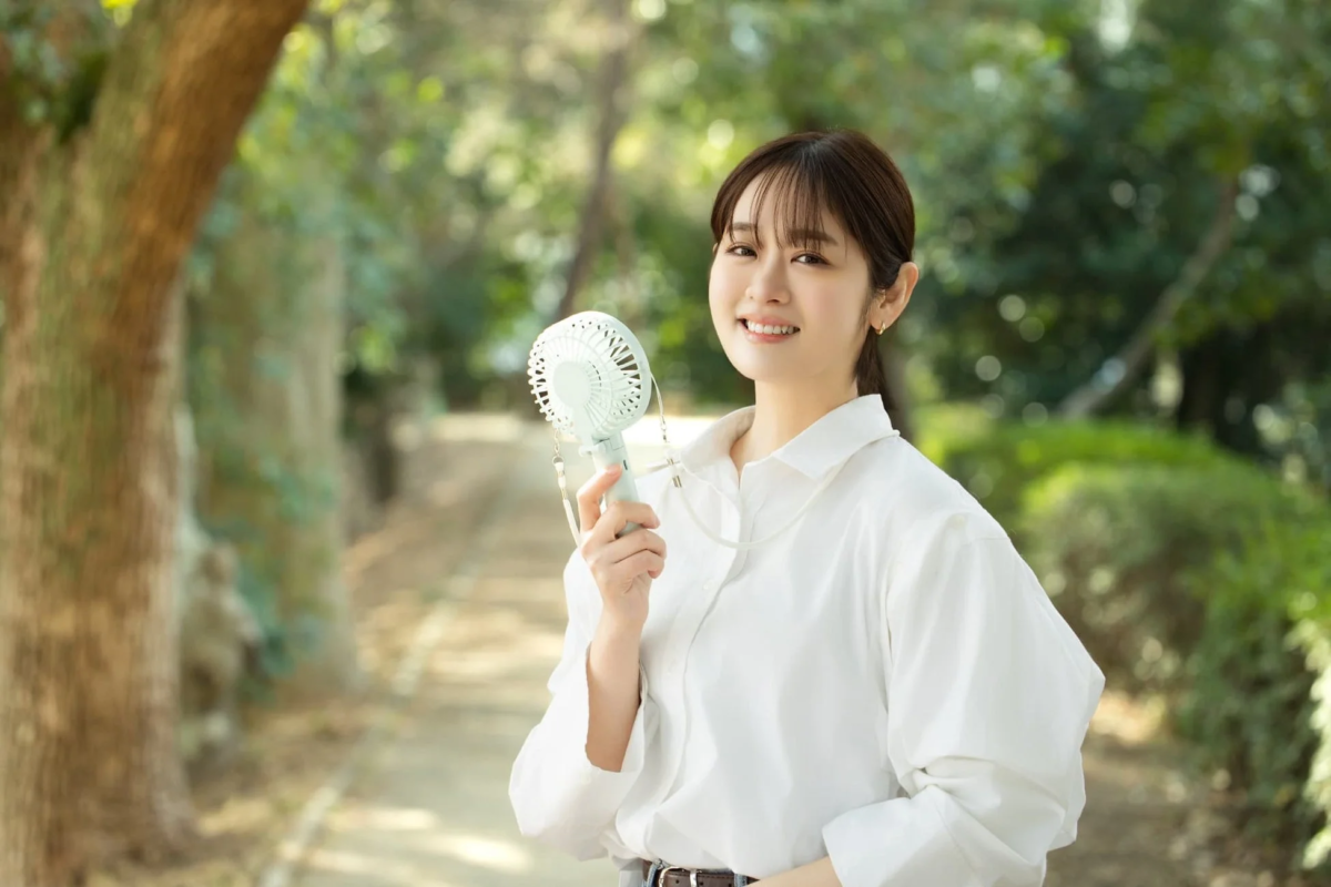 Woman using handheld fan outdoors