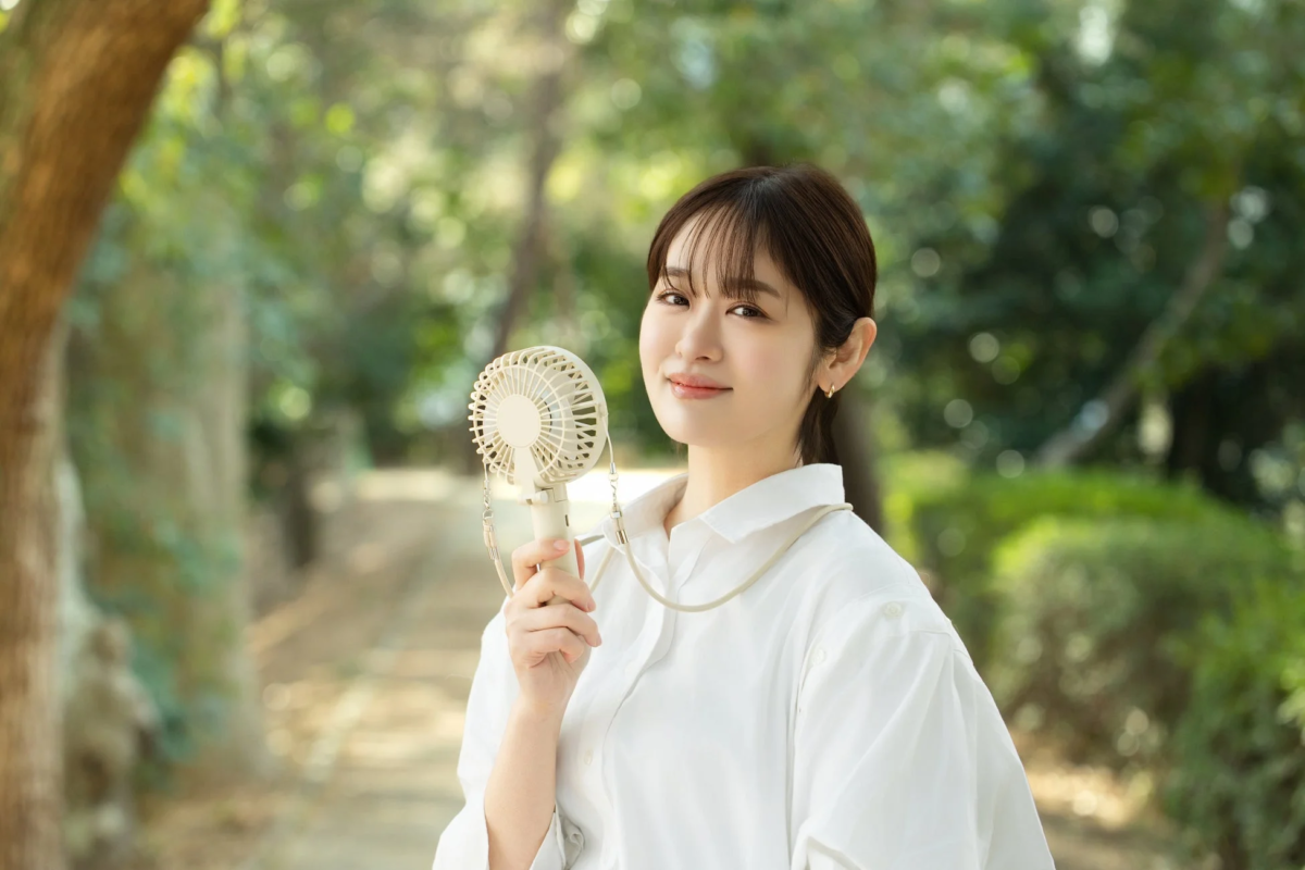 Woman smiling with handheld fan outdoors