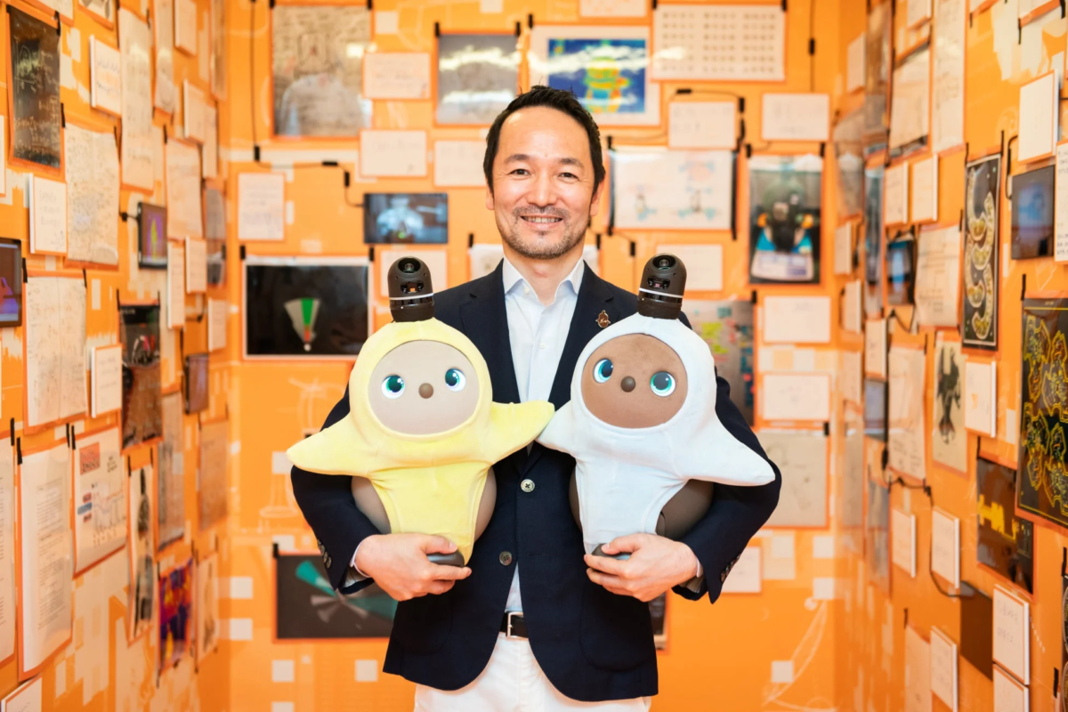 Smiling man holding two cute robots in an office setting