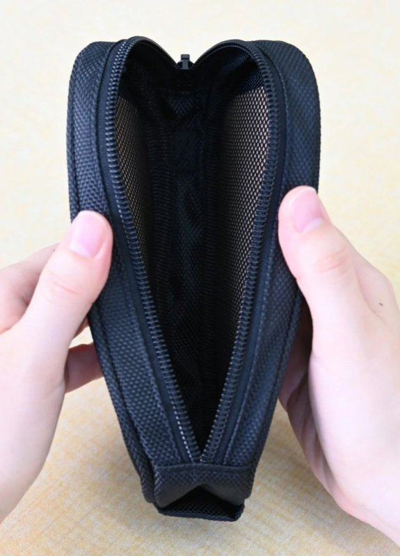 A black zippered pouch being opened with both hands. The interior of the pouch is made of mesh material.