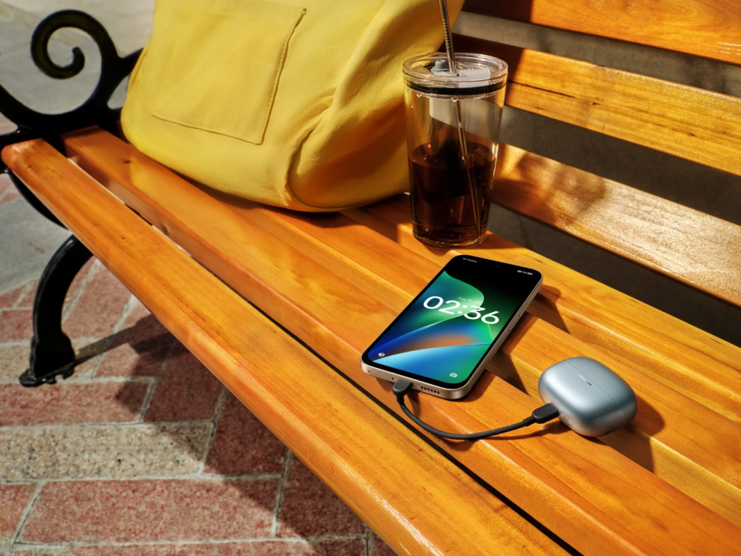 Smartphone charging wireless earphones on a bench